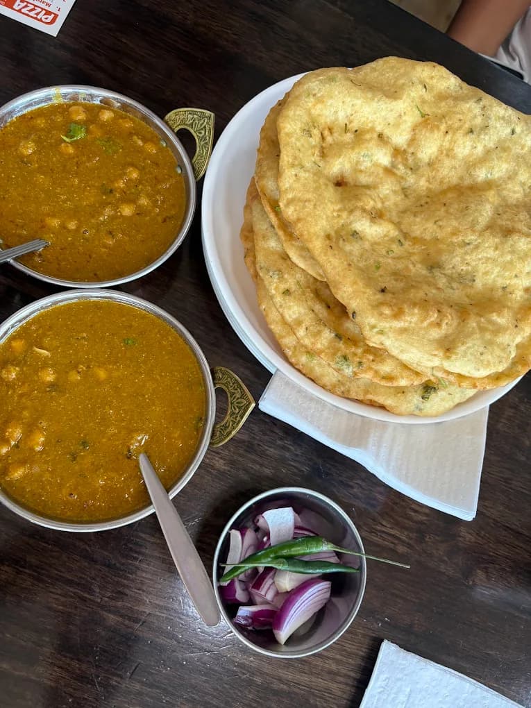 Two bowls of chickpea curry, a stack of fried flatbreads, and sliced onions and chilies.