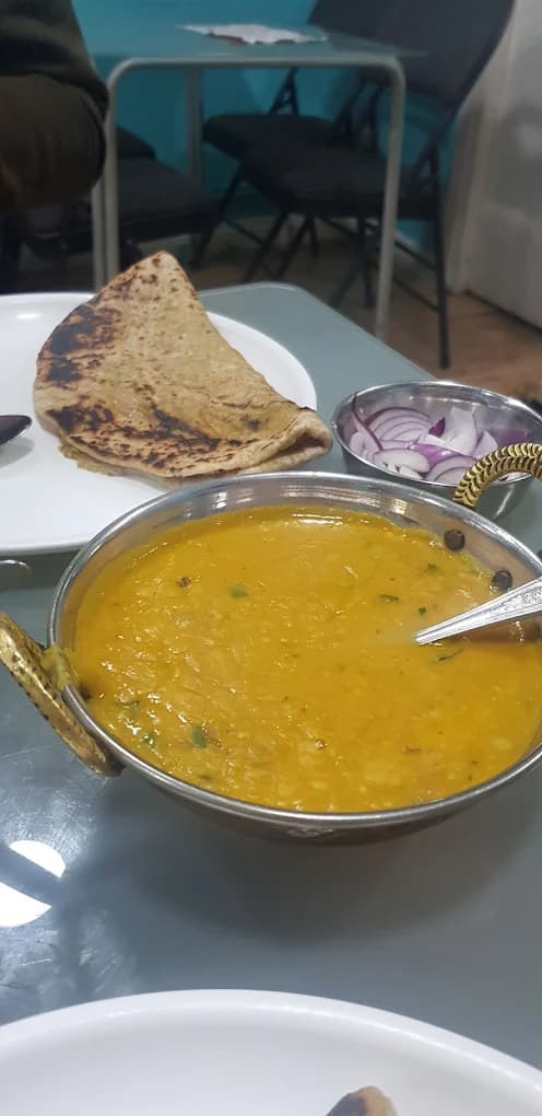 Yellow dal in a metal bowl served with toasted flatbread and sliced red onions.