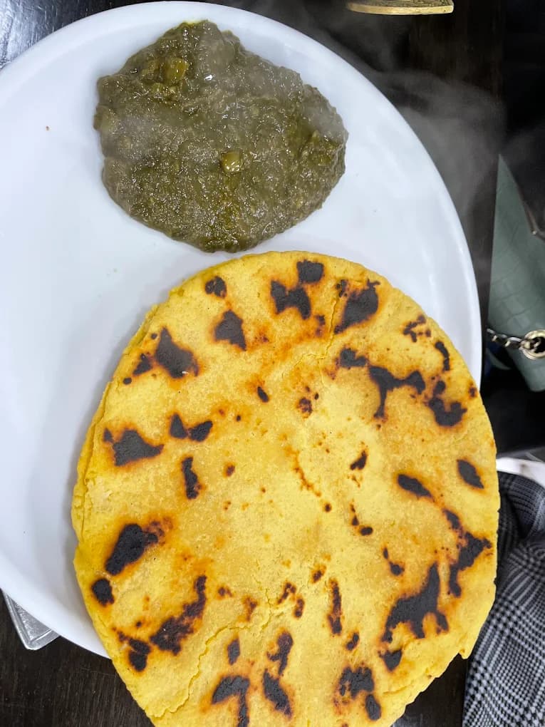 Charred yellow corn flatbread served with thick green mustard leaf puree on a plate.