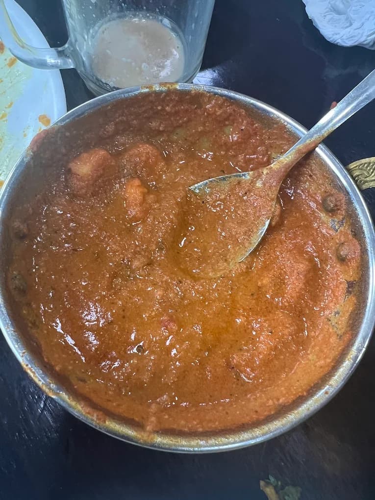 Rich, reddish-orange curry in a metal bowl with a silver spoon resting inside.